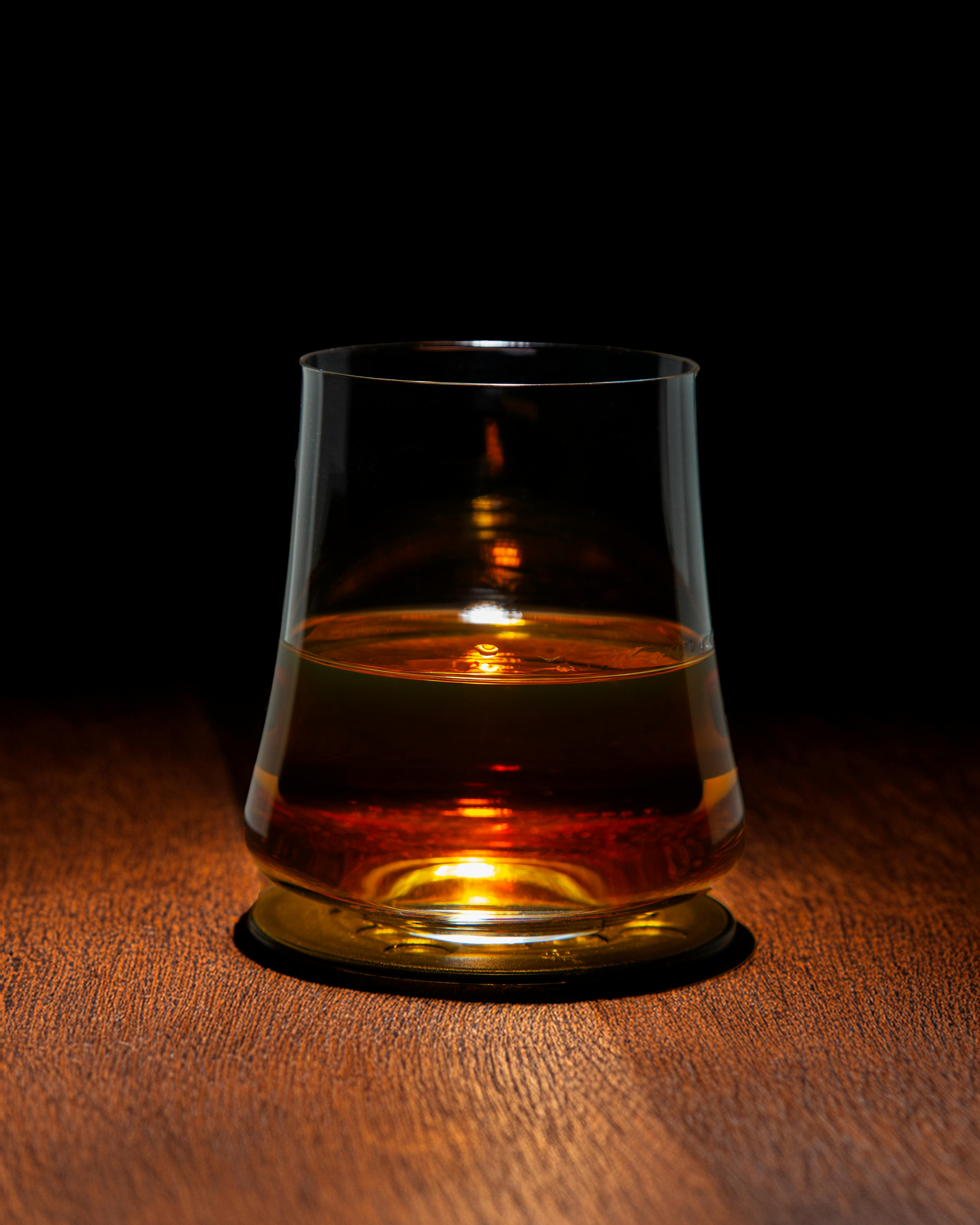 A tumbler glass filled with dark brown whisky with small ice cubes on the surface. On top of the glass lies a sprig of thyme.